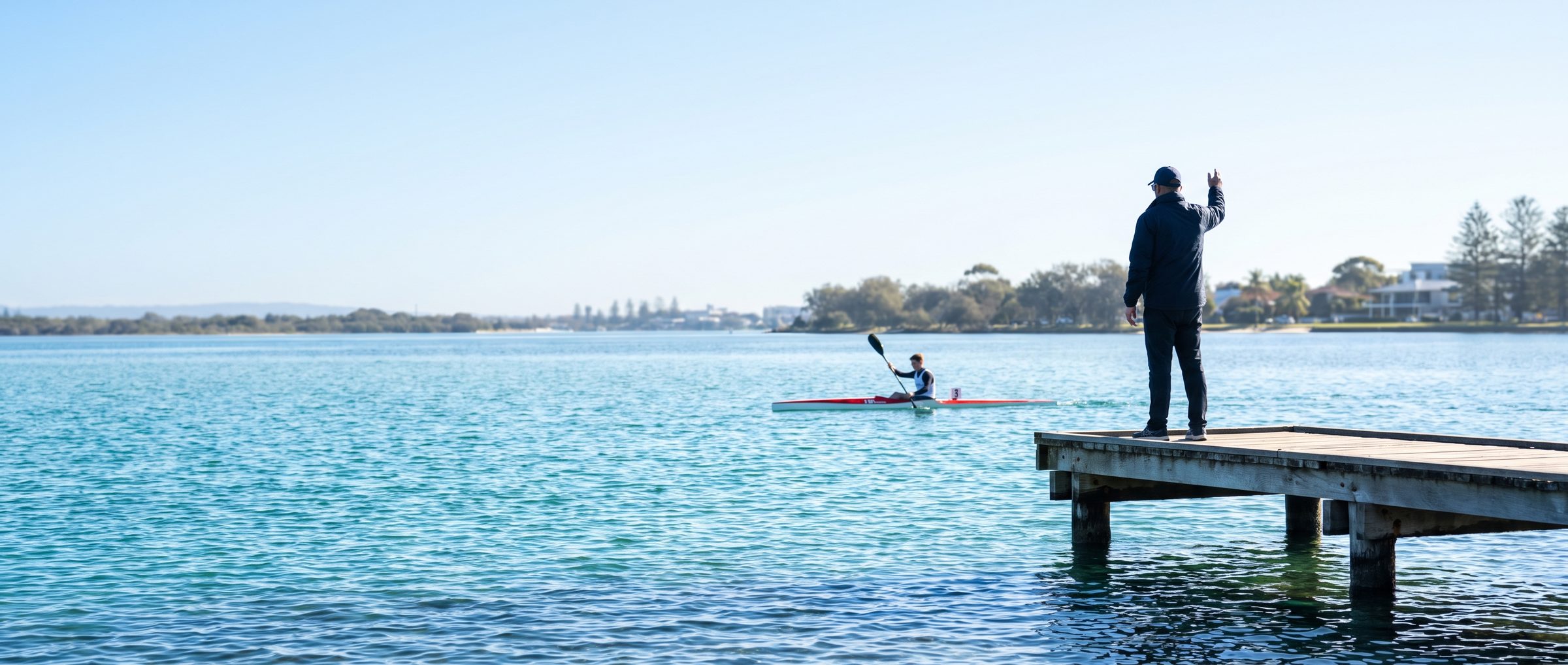 A coach on a pontoon directing a sprint kayak on calm water